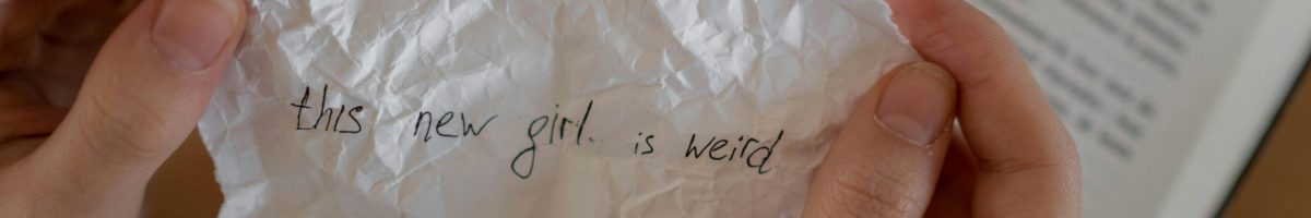 Close-up of hands holding a crumpled note with a handwritten message over an open book.